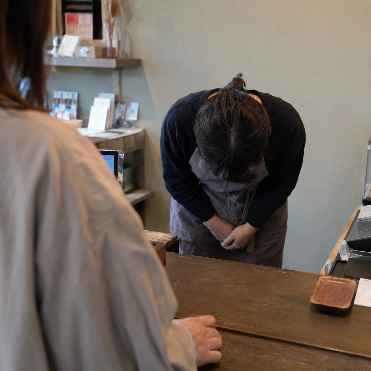 カウンター越しに客へ頭を下げて謝る店主
